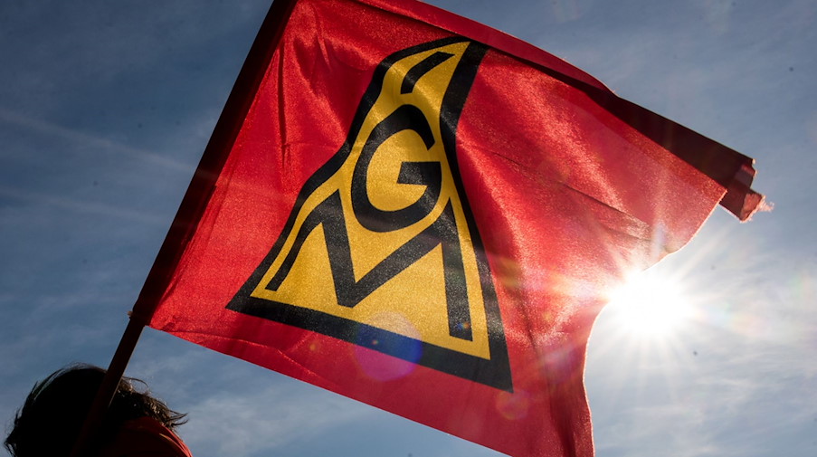 Teilnehmer einer Kundgebung halten eine Fahne mit dem Logo der IG Metall hoch. / Foto: Daniel Bockwoldt/dpa/Daniel Bockwoldt/Symbolbild