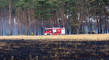 Ein Feuerwehrfahrzeug löscht am Waldrand den Brand. / Foto: Daniel Schäfer/dpa