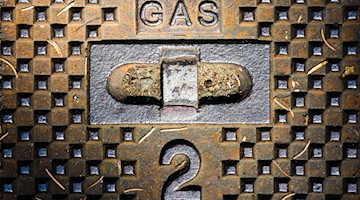 Ein Schriftzug „Gas“ und die Zahl 2 stehen auf einem gusseisernen Straßendeckel einer Gasleitung. / Foto: Julian Stratenschulte/dpa