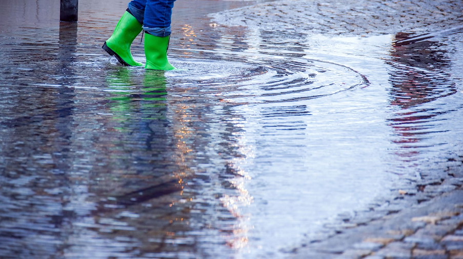 Mit Gummistiefeln geht eine Frau über eine leicht überflutete Straße. / Foto: Jens Büttner/dpa-Zentralbild/dpa/Symbolbild