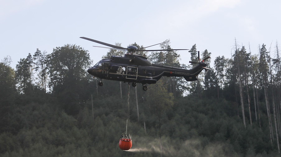 Ein Hubschrauber mit einem Wassertank für Löscharbeiten aus der Luft ist im Einsatz bei einem Waldbrand. / Foto: Christian Essler/xcitepress/dpa/Archivbild