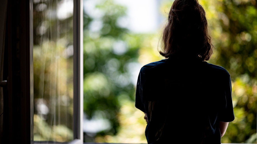 Eine Frau steht in ihrer Wohnung am Fenster. / Foto: Fabian Sommer/dpa/Illustration