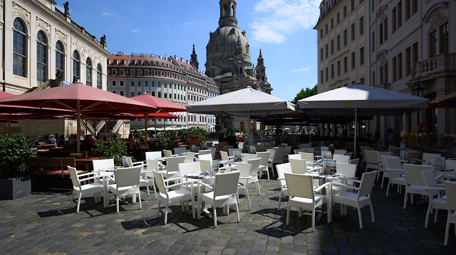 Stühle, Tische und Sonnenschirme eines Restaurants stehen auf dem Neumarkt vor der Frauenkirche. / Foto: Robert Michael/dpa