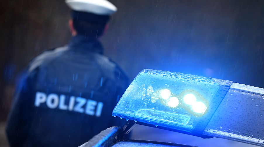 Ein Polizist steht im Regen vor einem Streifenwagen dessen Blaulicht aktiviert ist. / Foto: Karl-Josef Hildenbrand/dpa/Symbolbild