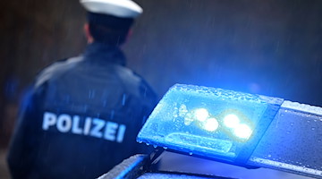 Ein Polizist steht im Regen vor einem Streifenwagen dessen Blaulicht aktiviert ist. / Foto: Karl-Josef Hildenbrand/dpa/Symbolbild