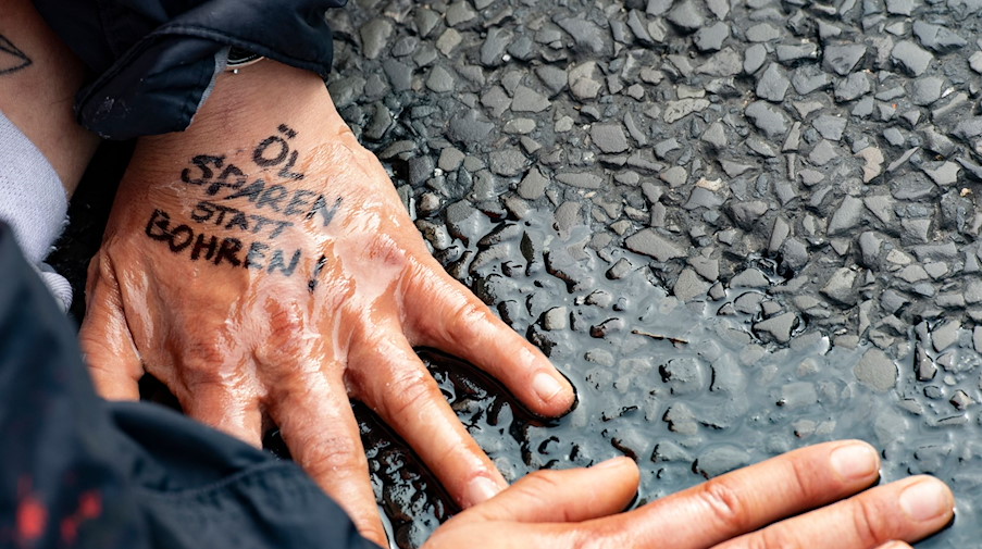 «Öl sparen statt bohren» steht auf der Hand einer Demonstrantin der Gruppe «Letzte Generation», die sich auf dem Asphalt festgeklebt hat. / Foto: Paul Zinken/dpa/Symbolbild