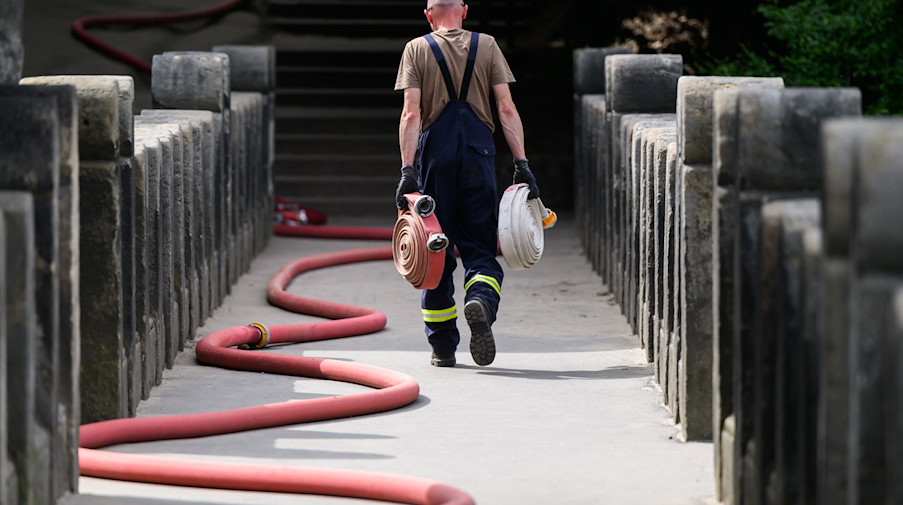 Ein Feuerwehrmann läuft mit zusammengerollten Schläuchen über die Basteibrücke. / Foto: Robert Michael/dpa/Archivbild