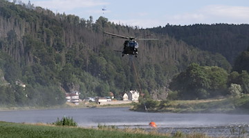 Ein Hubschrauber der Bundeswehr fliegt mit einem Löschwasser-Außenlastbehälter über der Elbe. / Foto: Sebastian Kahnert/dpa