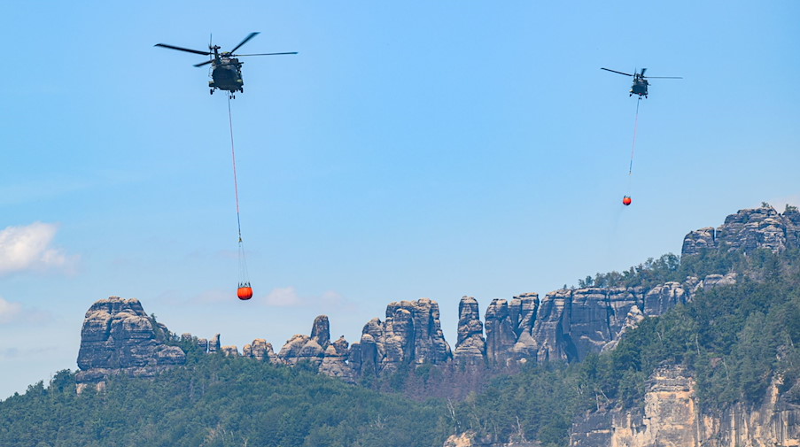 Hubschrauber der Bundeswehr fliegen mit Löschwasser-Außenlastbehältern um einen Waldbrand. / Foto: Robert Michael/dpa