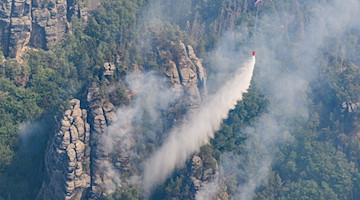 Ein Lastenhubschrauber wirft Löschwasser über einem Wald im Nationalpark Sächsische Schweiz ab. / Foto: Robert Michael/dpa