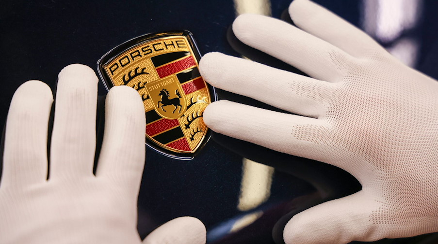 Ein Mitarbeiter befestigt das Wappen an einem Porsche Macan im Leipziger Porsche Werk. / Foto: Jan Woitas/dpa-Zentralbild/dpa/Archivbild