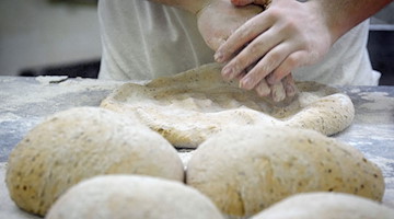Ein Bäcker formt in der Backstube auf einer mit Mehl bestäubten Arbeitsplatte den Teig. / Foto: Soeren Stache/dpa/Symbolbild