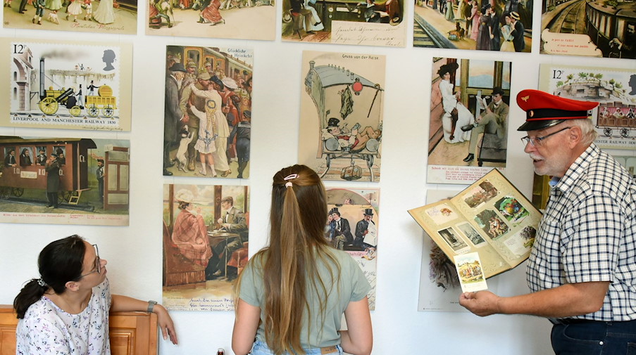 Günther Hunger zeigt Besucherinnen die Ausstellung in seinem Eisenbahn-Postkarten-Museum in Oschatz. / Foto: Waltraud Grubitzsch/dpa/Archivbild