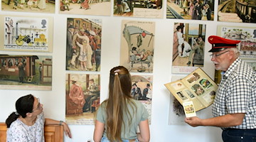 Günther Hunger zeigt Besucherinnen die Ausstellung in seinem Eisenbahn-Postkarten-Museum in Oschatz. / Foto: Waltraud Grubitzsch/dpa/Archivbild