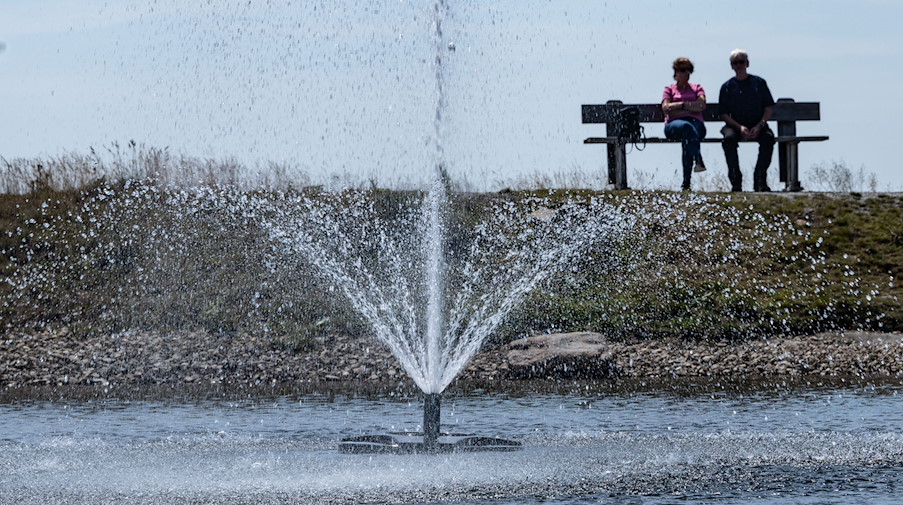 Touristen sitzen auf einer Bank hinter einem Springbrunnen. / Foto: Swen Pförtner/dpa/Symbolbild
