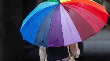 Eine Frau schützt sich bei Regen mit einem bunten Schirm. / Foto: Peter Kneffel/dpa/Symbolbild