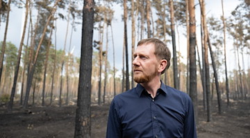 Michael Kretschmer begutachtet die Schäden in einem an Brandenburg angrenzenden Waldbrandgebiet bei Arzberg. / Foto: Sebastian Kahnert/dpa