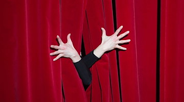 Die Hände einer Schauspielerin lugen bei der Probe hinter dem roten Vorhang hervor. / Foto: Sebastian Kahnert/dpa-Zentralbild/dpa/Symbolbild