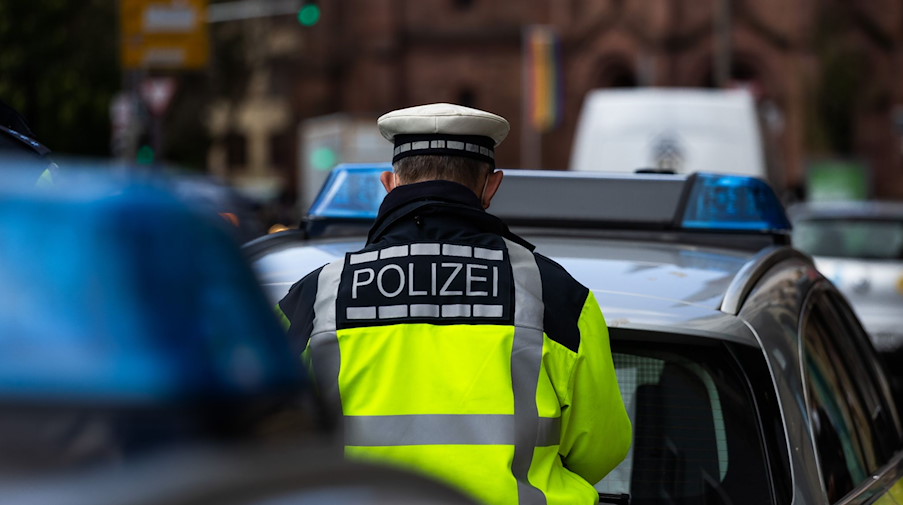 Ein Polizeibeamter steht zwischen zwei Einsatzfahrzeugen der Polizei. / Foto: Philipp von Ditfurth/dpa/Symbolbild