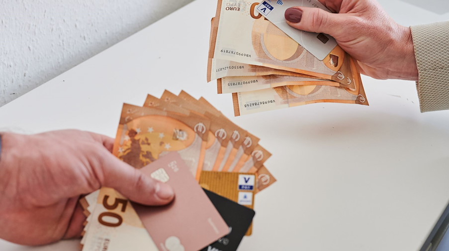 Ein Mann (l) und eine Frau halten unterschiedlich viele Geldscheine und Karten in der Hand. / Foto: Annette Riedl/dpa/Illustration