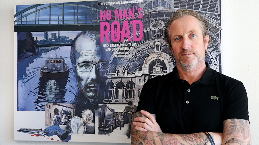 Autor und Regisseur Maik Große Lochtmann steht vor dem Filmplakat für "No Man's Road". / Foto: Roland Weihrauch/dpa