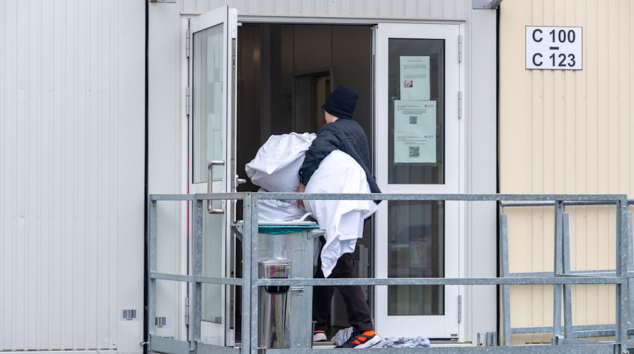 Ein Mann geht mit Bettzeug in einen Container mit Wohnbereichen in einer Aufnahmeeinrichtung. / Foto: Harald Tittel/dpa/Symbolbild