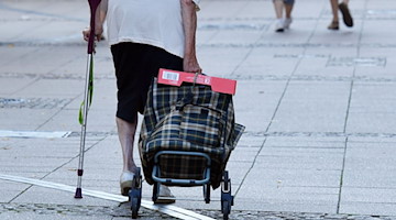 Eine alte Frau mit einer Krücke und Einkaufstrolley geht durch eine Fußgängerstraße. / Foto: Jens Kalaene/dpa/Archivbild