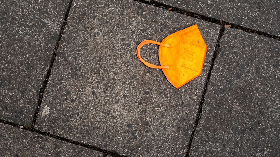 Ein gebrauchter orangefarbener Mund-Nasen-Schutz liegt auf dem Gehweg. / Foto: Peter Kneffel/dpa/Symbolbild