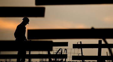 Die Silhouette eines Bauarbeiters zeichnet vor dem Morgenhimmel ab. / Foto: Julian Stratenschulte/dpa/Symbolbild