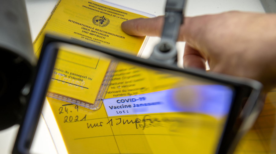 Bei der Kriminalpolizeiinspektion liegen Impfpässe unter einer Lupe, darunter ein aufgeschlagener Impfausweis. / Foto: Stefan Puchner/dpa/Archivbild