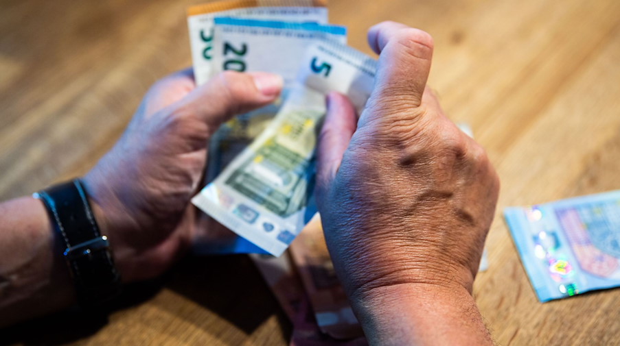 Ein älterer Mann zählt Geld an einem Tisch. / Foto: Lino Mirgeler/dpa/Illustration