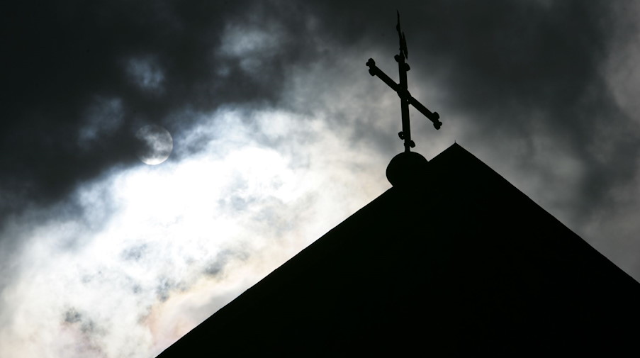 Im Gegenlicht und vor wolkenverhangenem Himmel ist die Kirchturmspitze des Doms mit Kreuz zu sehen. / Foto: Friso Gentsch/dpa/Symbolbild