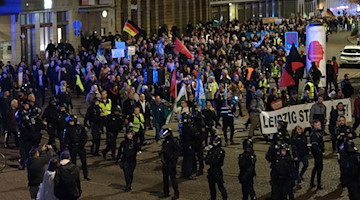 Teilnehmer einer Demonstration gehen mit Transparenten und Fahnen eine Straße in Leipzig entlang. / Foto: Sebastian Willnow/dpa