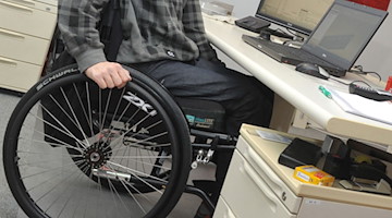 Ein Mann sitzt in einem Rollstuhl an seinem Arbeitsplatz am Schreibtisch. / Foto: Stefan Puchner/dpa