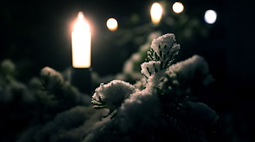 Mit Schnee bedeckt sind die Zweige eines mit Lichtern geschmückten Christbaumes. / Foto: Karl-Josef Hildenbrand/dpa/Symbolbild
