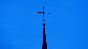 Das Kreuz einer Kirche ist in der Abenddämmerung zu sehen. / Foto: Friso Gentsch/dpa/Archivbild