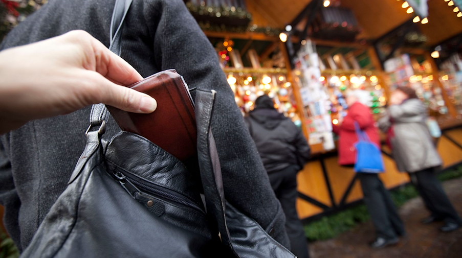 Ein Mann zieht auf dem Weihnachtsmarkt einer Besucherin die Geldbörse aus der Handtasche. / Foto: Frank Rumpenhorst/dpa/Archiv