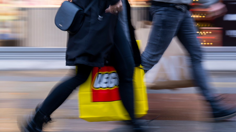 Eine Frau und ein Mann mit großen Einkaufstaschen gehen über eine Einkaufsstraße. / Foto: Monika Skolimowska/dpa/Archivbild