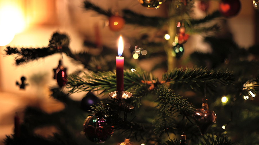 Eine Kerze brennt an einem festlich geschmückten Weihnachtsbaum. / Foto: Karl-Josef Hildenbrand/dpa/Symbolbildarchiv