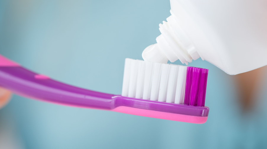 Eine Frau drückt eine Zahnpastatube über einer Zahnbürste aus. / Foto: Christin Klose/dpa-tmn/Symbolbild