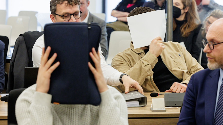 Zwei Angeklagte bedecken ihre Gesichter im Gerichtssaal des Oberlandesgerichts. / Foto: Jens Schlueter/POOL AFP/dpa/Archivbild