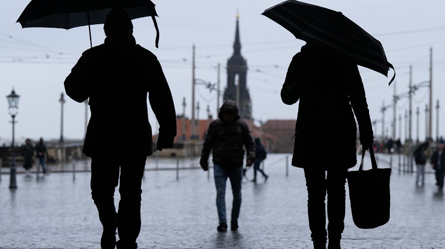 Passantinnen und Passanten gehen bei Regen und mit Regenschirm vor der Augustusbrücke. / Foto: Sebastian Kahnert/dpa