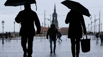 Passantinnen und Passanten gehen bei Regen und mit Regenschirm vor der Augustusbrücke. / Foto: Sebastian Kahnert/dpa