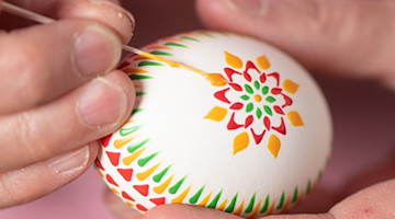 Mit einem selbst gefertigten Feder-Pinsel wird farbiges heißes Wachs auf das Ei aufgetragen. / Foto: Sebastian Kahnert/dpa/Archivbild