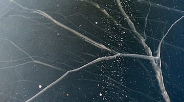 Risse durchziehen die Eisschicht auf einem zugefrorenen See. / Foto: Patrick Pleul/dpa-Zentralbild/dpa/Symbolbild