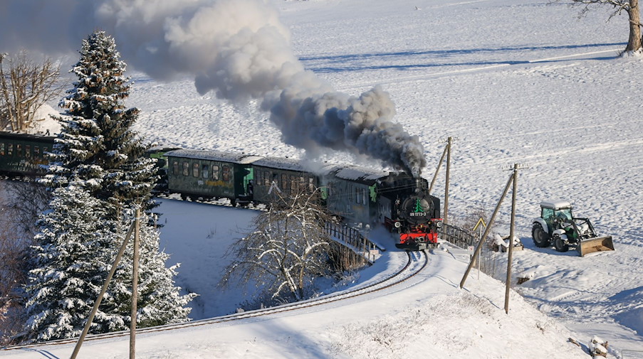Mit reichlich Rauch und Qualmwolken bahnt sich die Fichtelbergbahn ihren Weg durch das verschneite Erzgebirge. / Foto: Jan Woitas/dpa/Archivbild