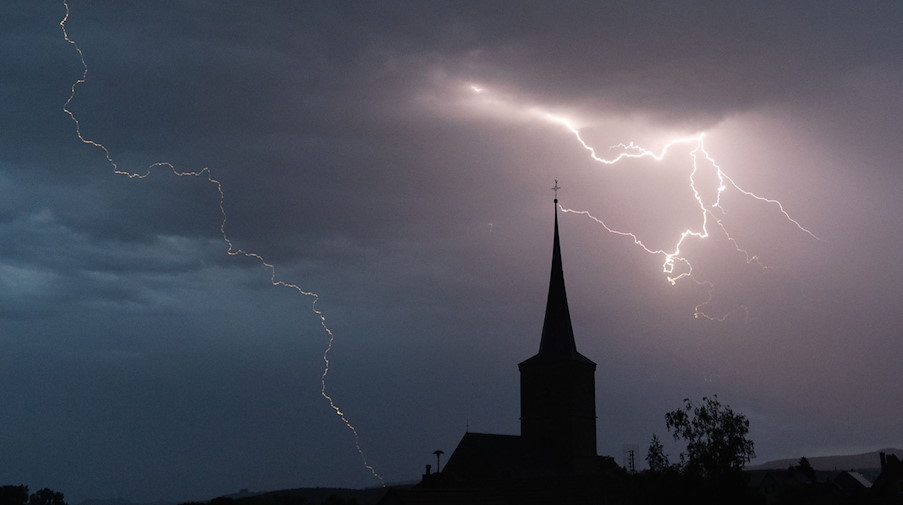 Blitze entladen sich hinter einer Kirche. / Foto: Nicolas Armer/dpa/Symbolbild
