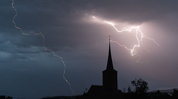 Blitze entladen sich hinter einer Kirche. / Foto: Nicolas Armer/dpa/Symbolbild