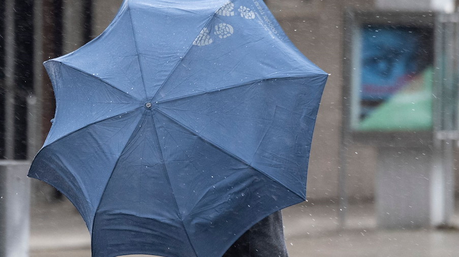 Bei Regenwetter läuft ein Passant mit Regenschirm durch die Stadt. / Foto: Boris Roessler/dpa/Symbolbild