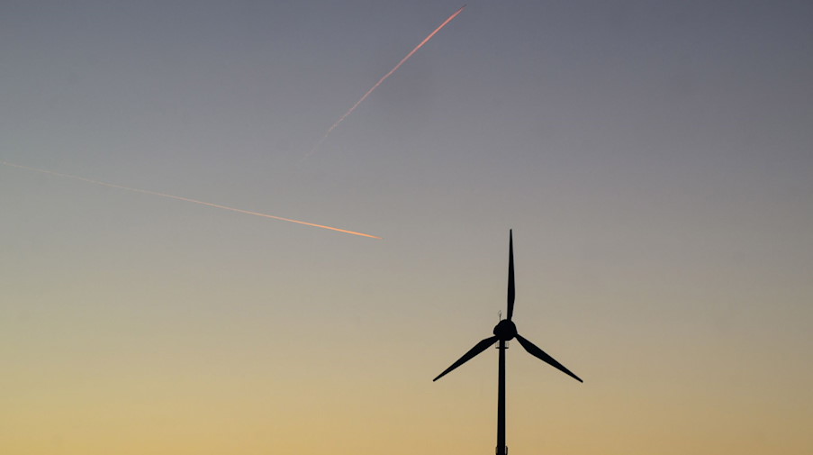 Zwei Flugzeuge ziehen Kondensstreifen am Himmel über einer Windkraftanlage. / Foto: Julian Stratenschulte/dpa/Archivbild